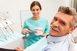 Patient smiling with dentist in background demonstrating brushing teeth
