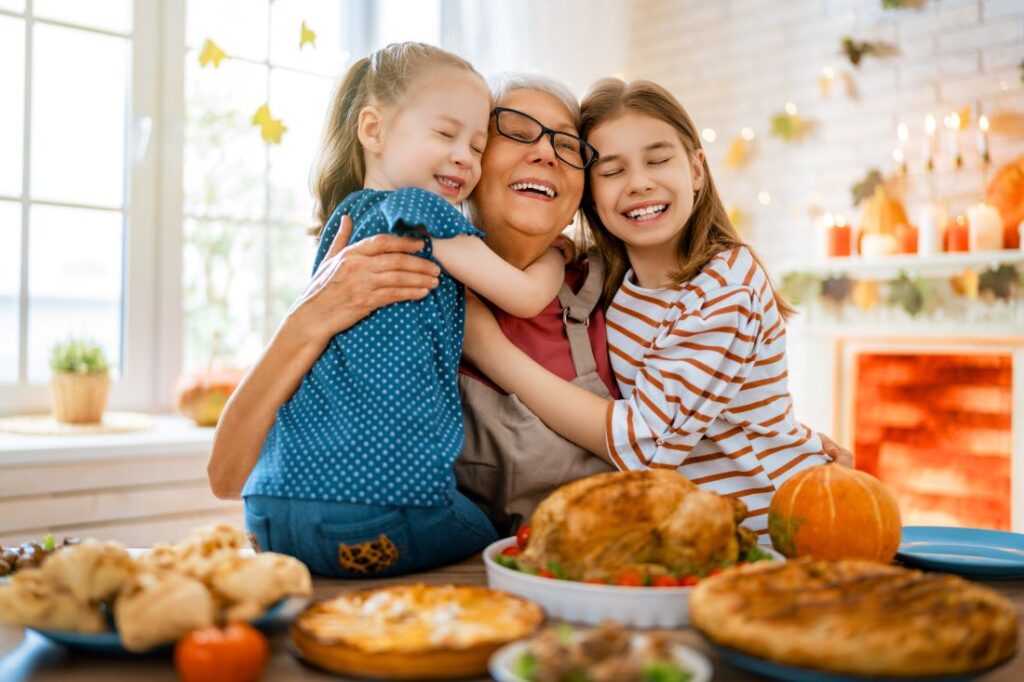 A woman and two children embracing in front of a table of Thanksgiving food.